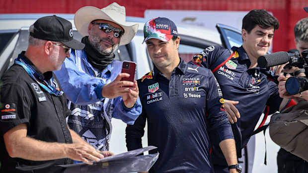 Checo Pérez mira la pantalla de un celular de un señor con lentes